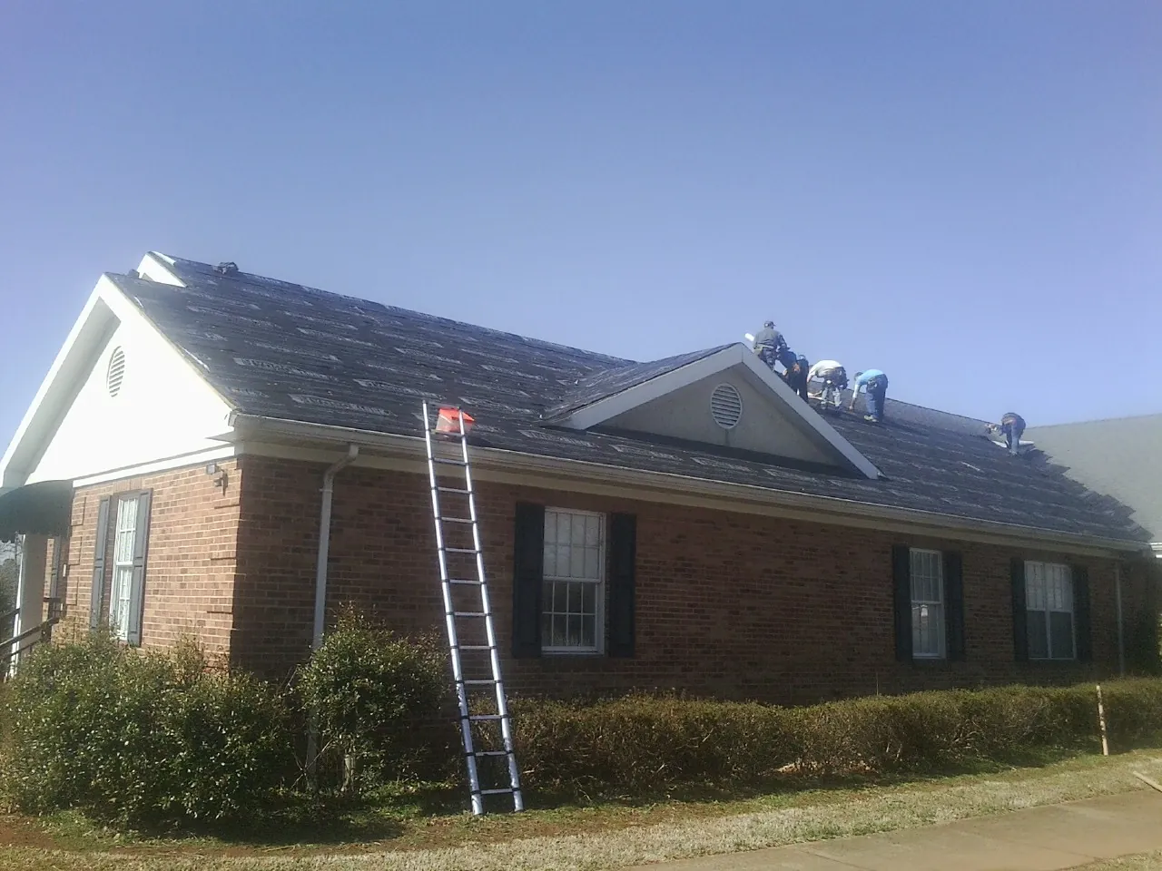 Crew tearing shingles off a brick ranch roof with a ladder set — Metal Roof Repair work by our crew in Sunbury