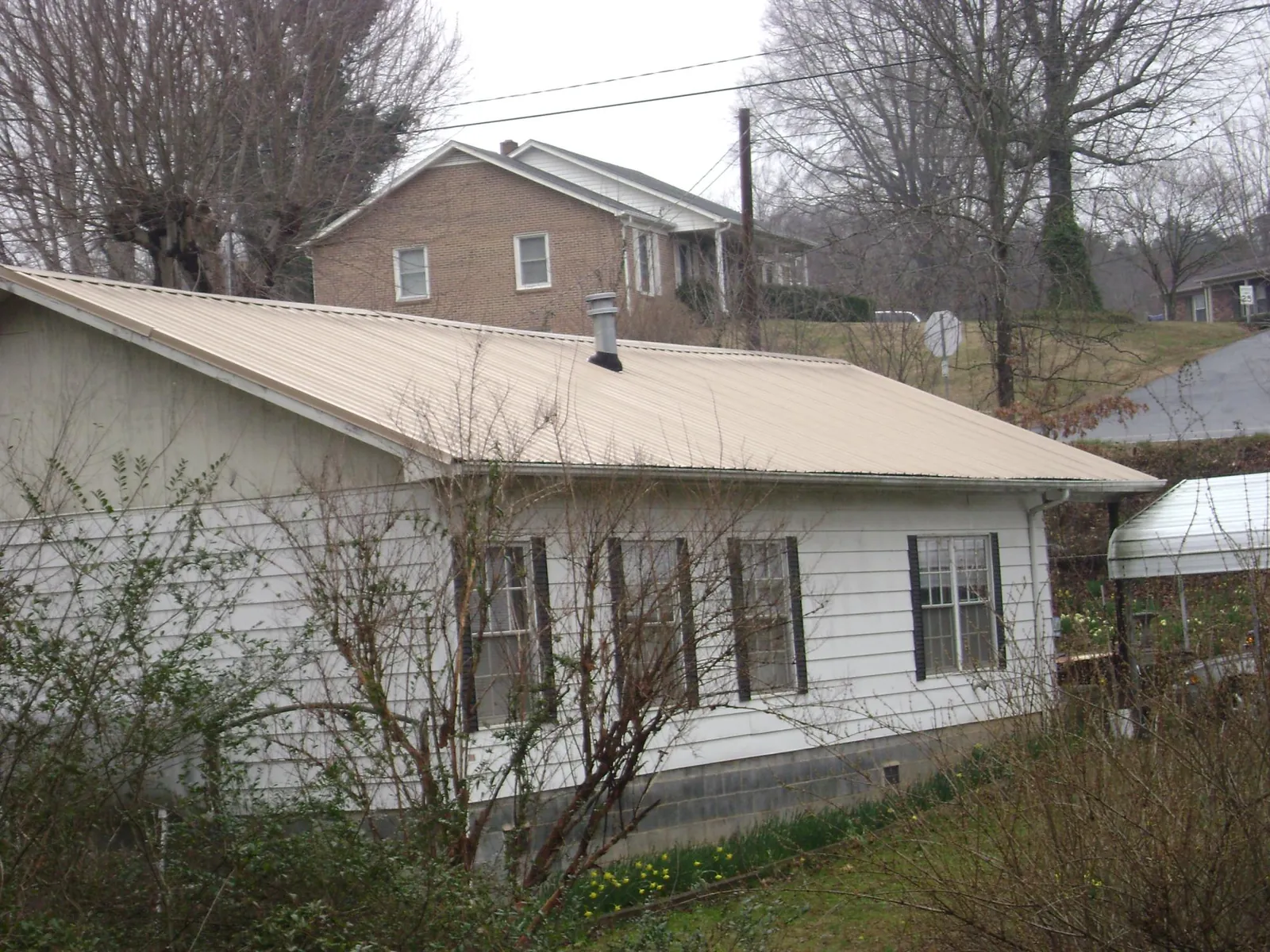 Tan metal roof on a white sided house set into a hillside — Commercial Roofing by Roofing Brothers in Sunbury